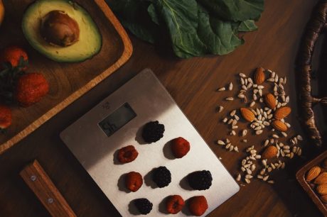 Top view of composed raw almond with seeds and avocado on table with berries on scales for cooking healthy dish
