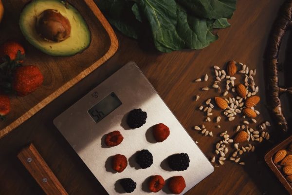 Top view of composed raw almond with seeds and avocado on table with berries on scales for cooking healthy dish