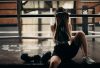A female boxer sitting in a gym ring, resting and wiping sweat with a towel after a workout.